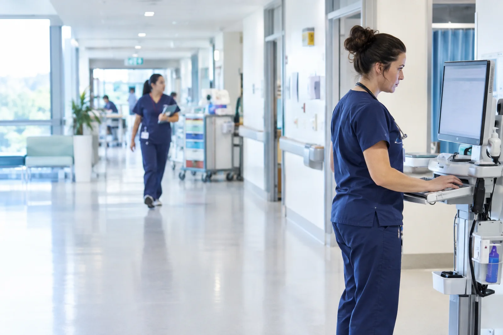 A clinician reviewing a record at a workstation on wheels in a hospital corridor.