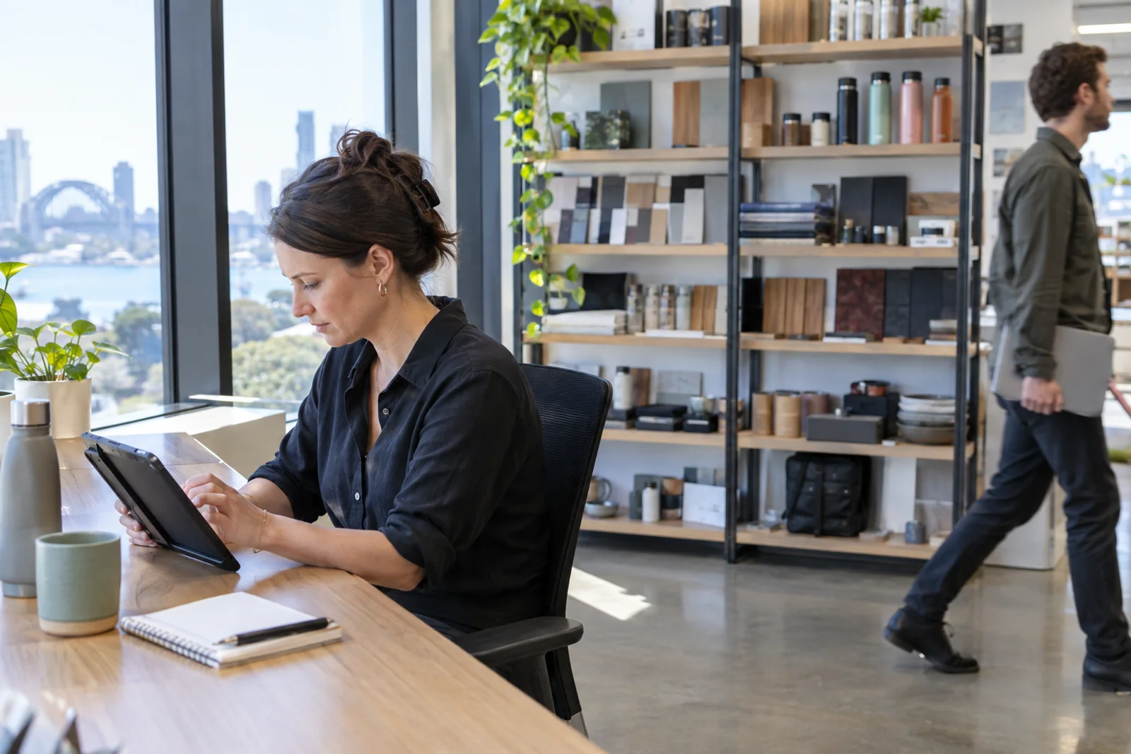 A customer operations manager at a window desk in a retail head office, reviewing a tablet.