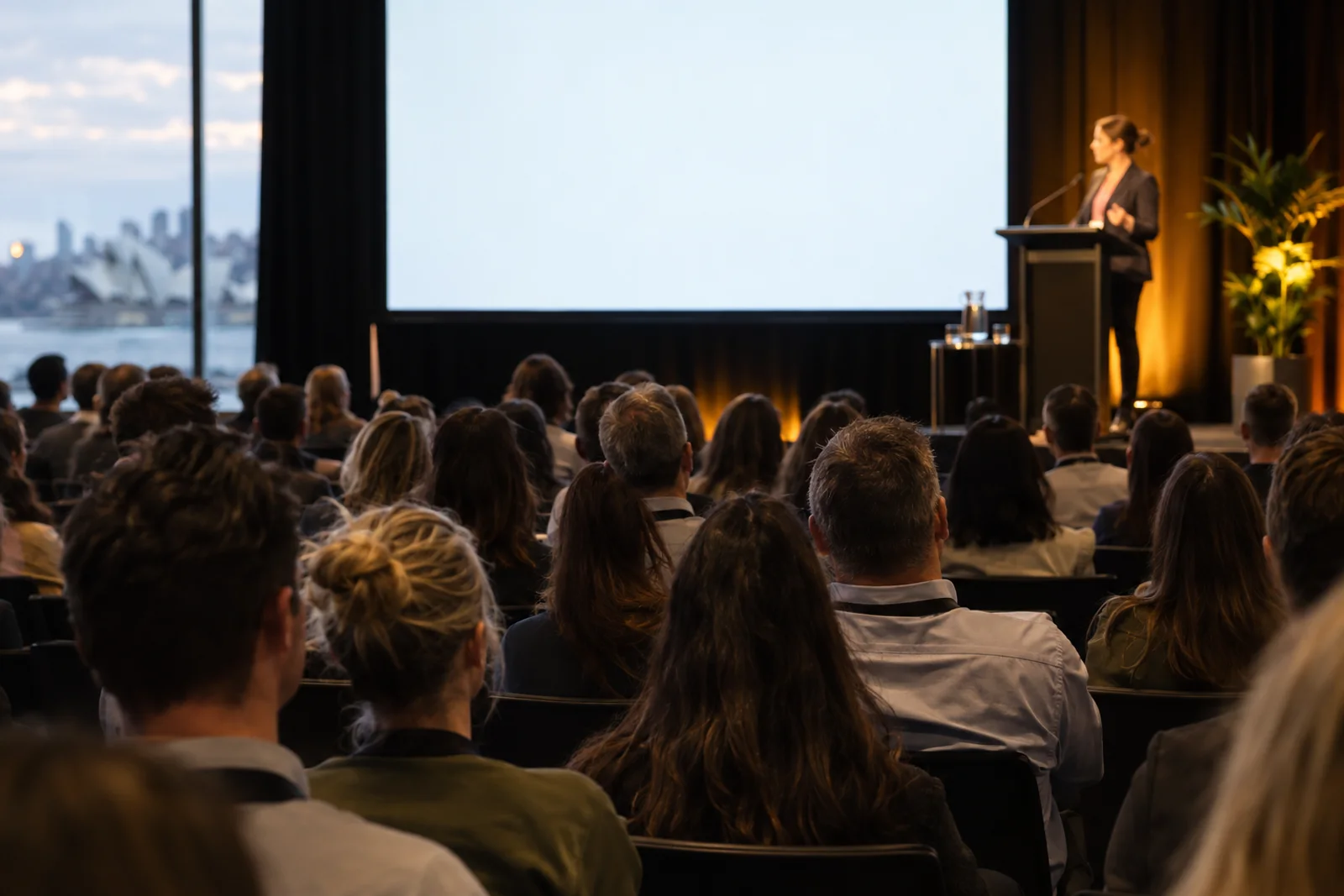 A speaker on stage at an industry event, seen over the audience.