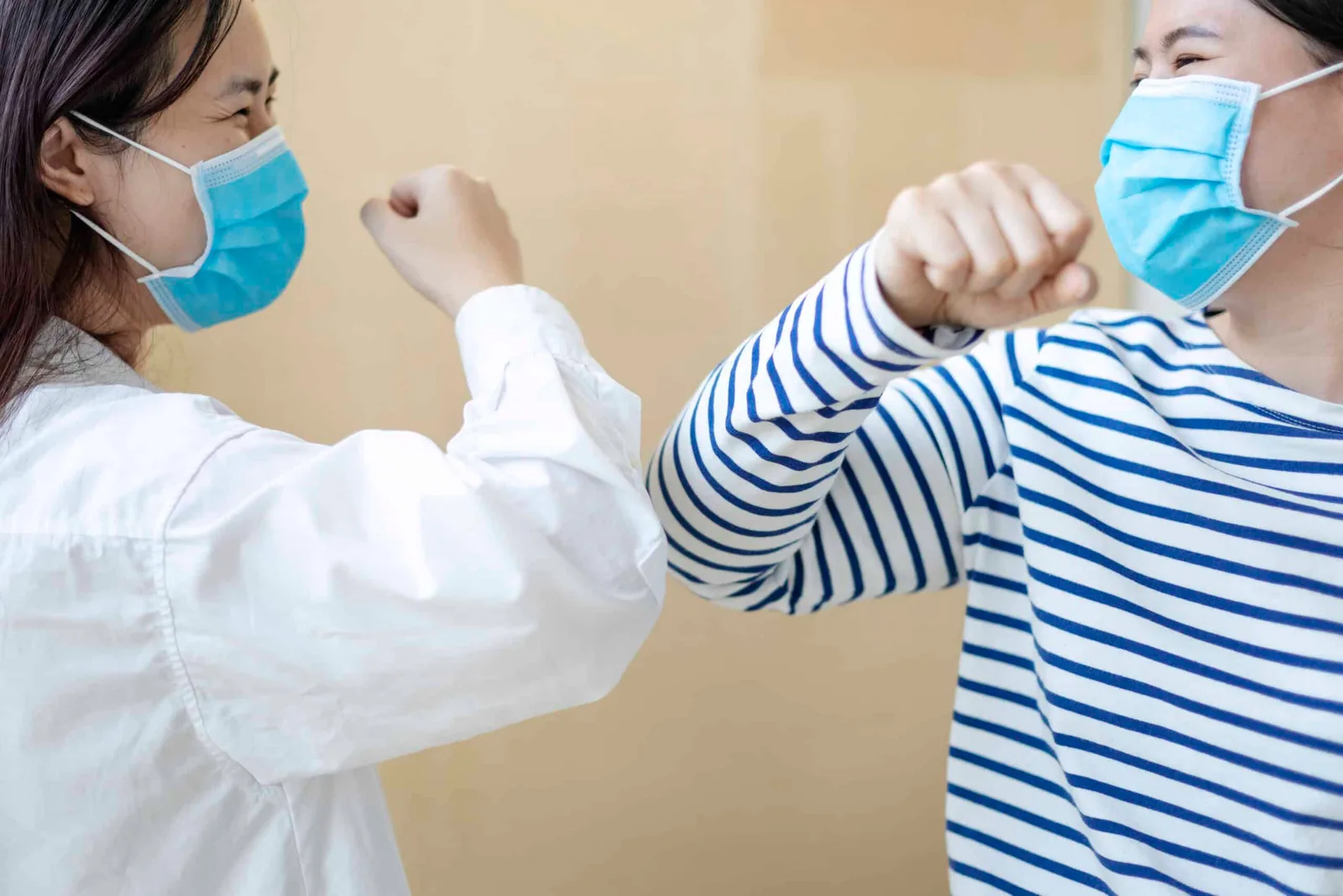 Two healthcare workers greeting each other in masks.