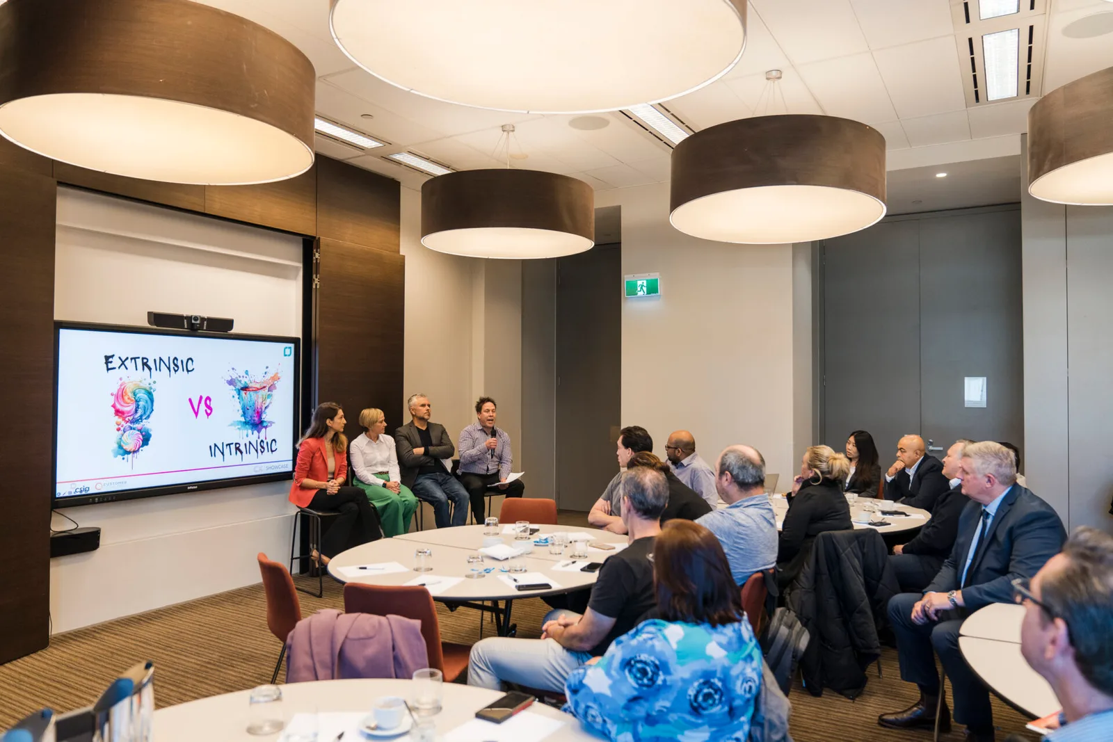 A wide conference room with a screen and attendees.